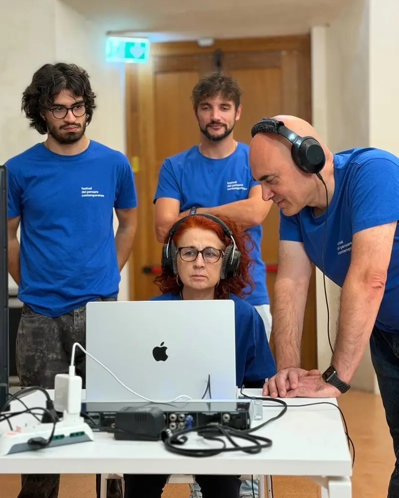A woman wearing headphones sits in front of a laptop connected to an audio interface; around her three people in the festival’s blue T-shirt, one of them listening on another pair of headphones.